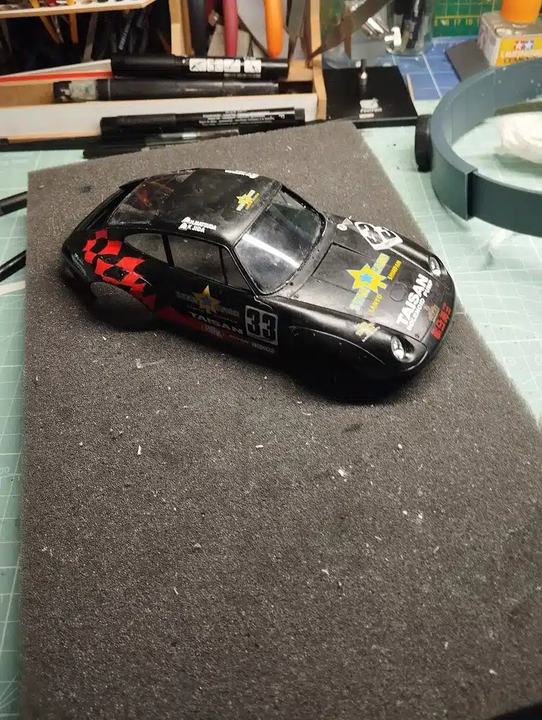 Maquette-de-voiture-de-course-noire-avec-le-numero-33-et-des-motifs-rouges-et-jaunes-posee-sur-une-surface-en-mousse-grise-avec-des-outils-de-modelisme-en-arriere-plan.jpg
26 octobre 2024